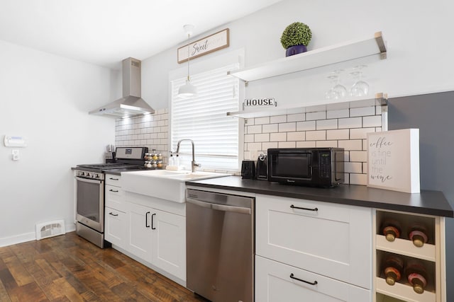 kitchen with stainless steel appliances, dark countertops, wall chimney exhaust hood, and open shelves