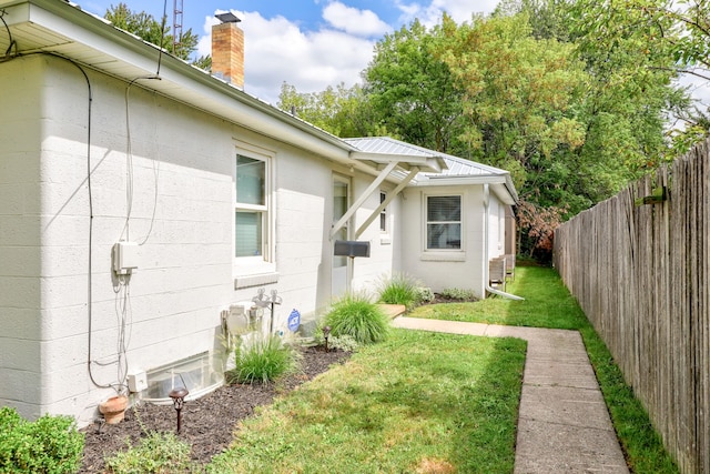 view of home's exterior featuring metal roof, a yard, concrete block siding, and fence