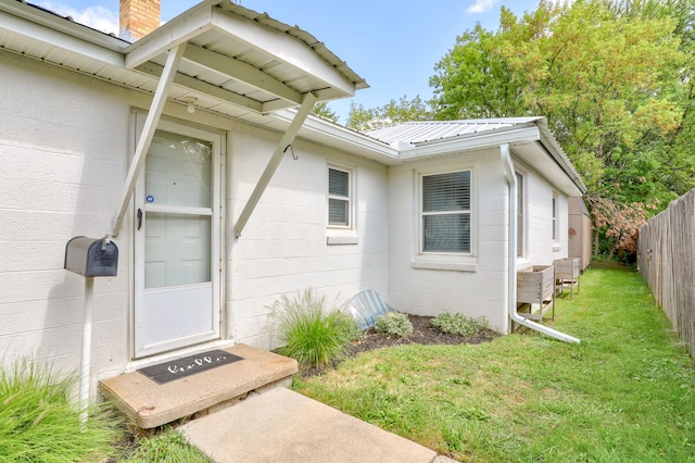 property entrance featuring metal roof, concrete block siding, fence, a yard, and a chimney