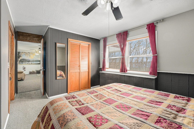 carpeted bedroom featuring a textured ceiling, ceiling fan, wood walls, and a closet