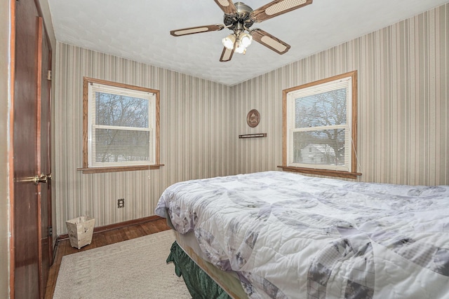 bedroom featuring wood finished floors, ceiling fan, baseboards, and wallpapered walls