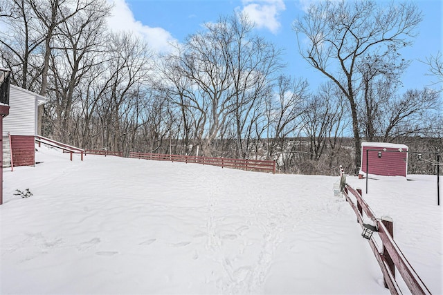 yard covered in snow with an outbuilding, a storage shed, and fence