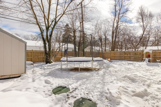 yard layered in snow with a trampoline and a fenced backyard