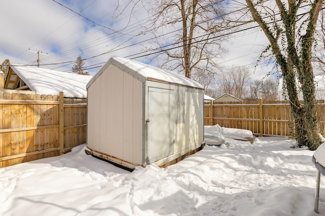 snow covered structure with an outbuilding, a storage unit, and a fenced backyard