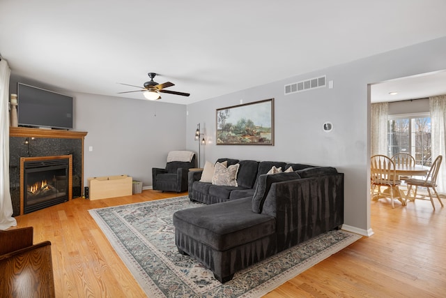 living area with baseboards, visible vents, a ceiling fan, a tiled fireplace, and light wood-style floors