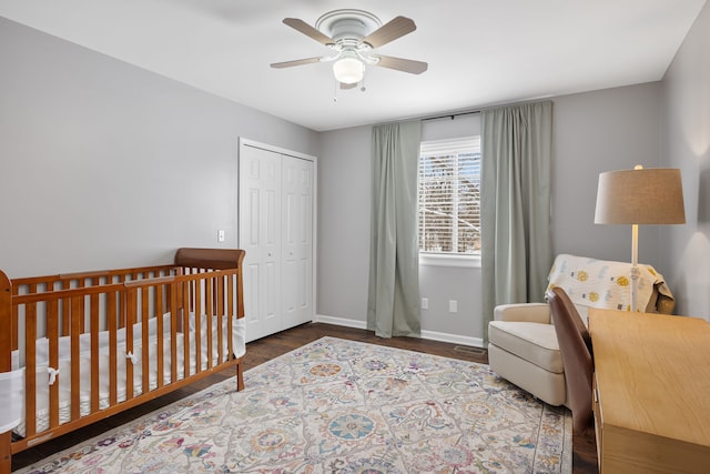 bedroom with a closet, a ceiling fan, wood finished floors, a nursery area, and baseboards