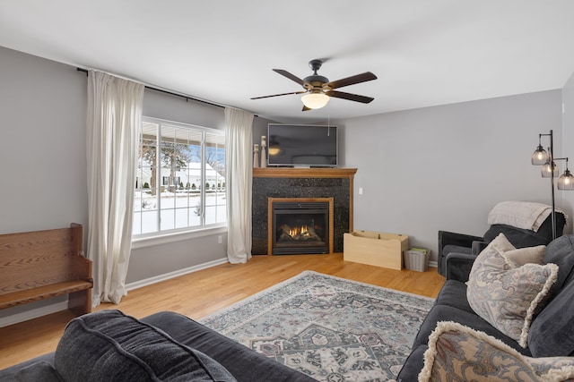 living area with ceiling fan, a premium fireplace, wood finished floors, and baseboards