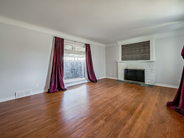 unfurnished living room featuring a glass covered fireplace, visible vents, baseboards, and wood finished floors