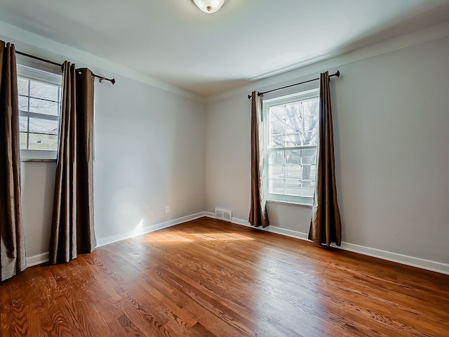 spare room featuring a wealth of natural light, visible vents, baseboards, and wood finished floors