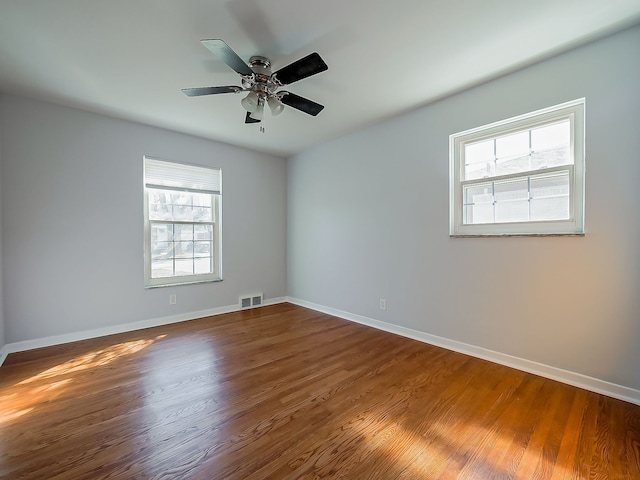 empty room with a ceiling fan, baseboards, visible vents, and wood finished floors