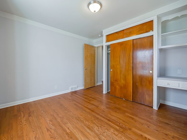 unfurnished bedroom with visible vents, baseboards, wood finished floors, and ornamental molding