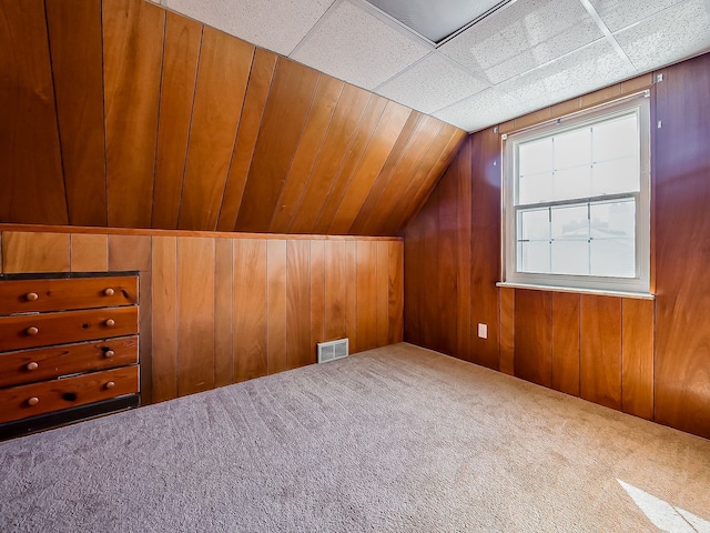 additional living space featuring carpet floors, wooden walls, visible vents, and lofted ceiling