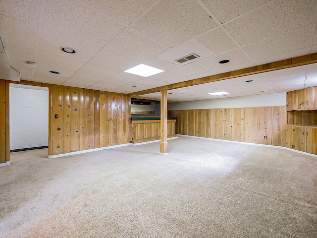 finished basement featuring wooden walls, visible vents, and carpet flooring