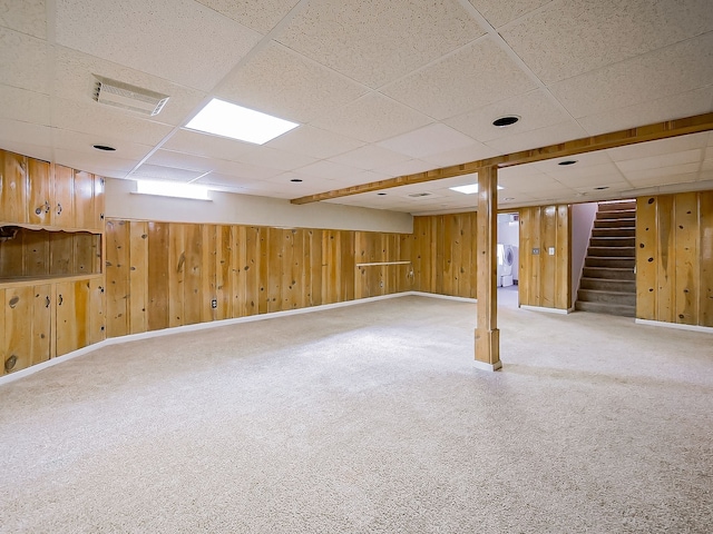 finished below grade area featuring a drop ceiling, carpet floors, wood walls, visible vents, and stairway