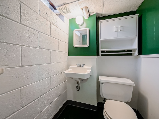 half bath with toilet, a sink, and concrete block wall