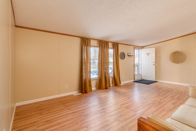 unfurnished living room featuring a textured ceiling, ornamental molding, baseboards, and light wood-style floors