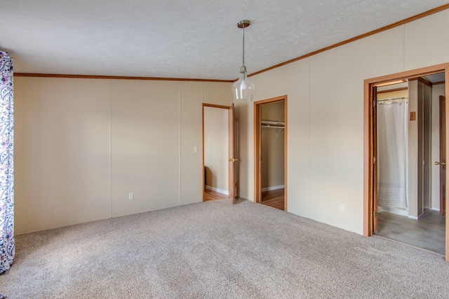 unfurnished bedroom featuring a textured ceiling, ensuite bathroom, crown molding, and carpet flooring