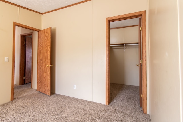 unfurnished bedroom with carpet, crown molding, a spacious closet, and a closet