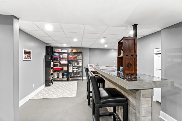 bar featuring a drop ceiling, recessed lighting, indoor bar, baseboards, and finished concrete flooring