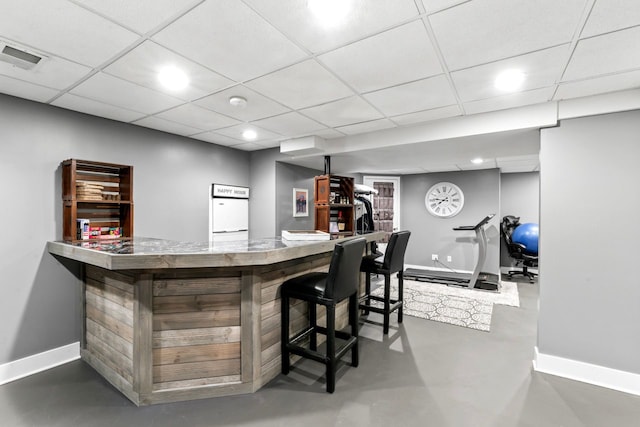 bar with a dry bar, baseboards, a drop ceiling, refrigerator, and finished concrete floors