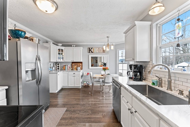 kitchen with white cabinets, ornamental molding, dark wood-style flooring, stainless steel appliances, and a sink