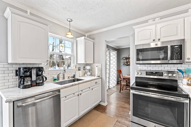 kitchen with light wood finished floors, white cabinets, appliances with stainless steel finishes, ornamental molding, and a sink