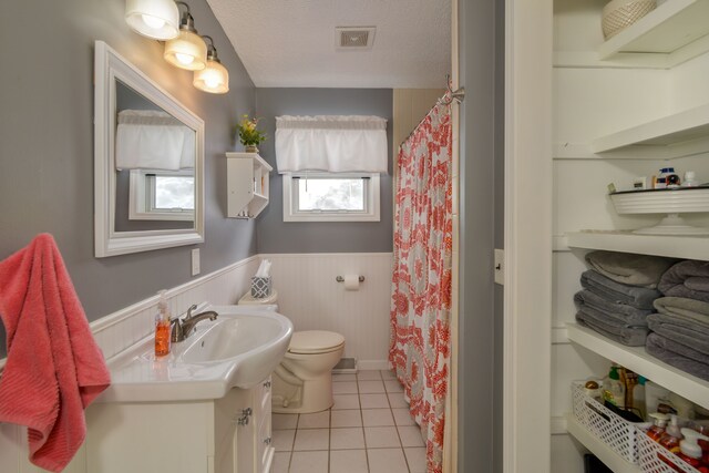7214 S M 66, Mancelona, MI 49659 - full bath featuring tile patterned floors, toilet, vanity, a textured ceiling, and wainscoting