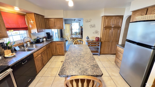 kitchen featuring light tile patterned floors, black dishwasher, dark countertops, freestanding refrigerator, and a sink