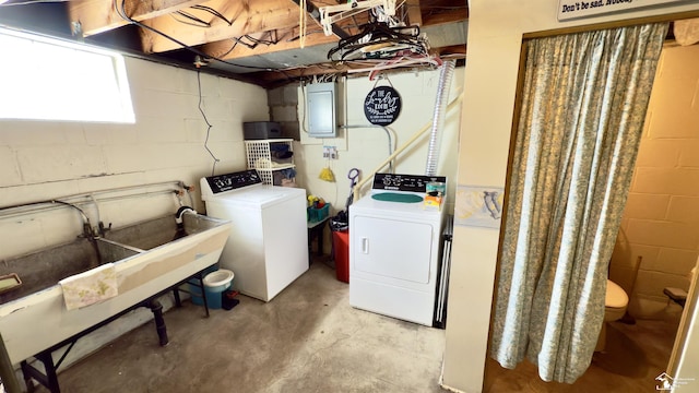 washroom with concrete block wall, laundry area, electric panel, washing machine and dryer, and a sink