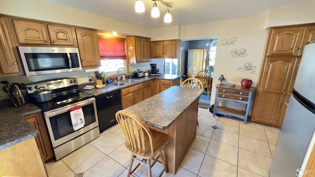 kitchen featuring light tile patterned floors, a kitchen island, appliances with stainless steel finishes, and a sink