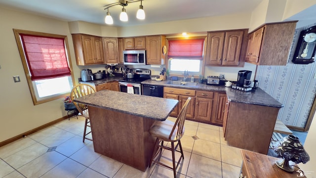 kitchen featuring stainless steel appliances, dark countertops, brown cabinetry, a sink, and a kitchen bar