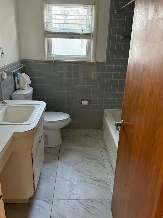 bathroom with toilet, vanity, tile walls, marble finish floor, and wainscoting