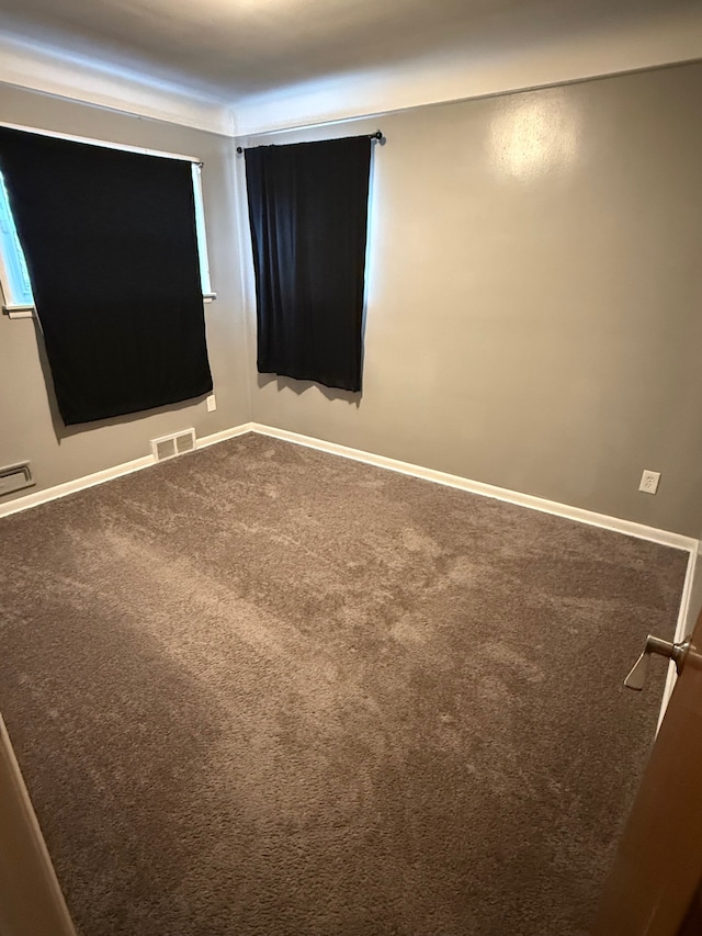 unfurnished room featuring visible vents, dark carpet, and baseboards