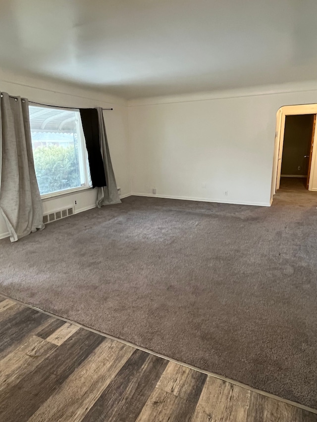 unfurnished room featuring dark wood-type flooring, visible vents, and dark carpet