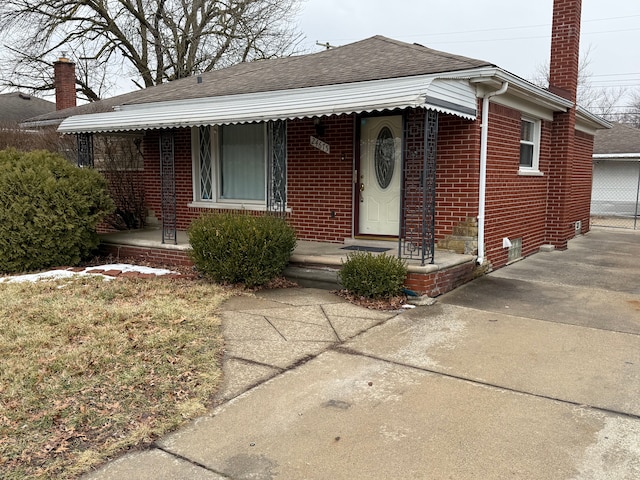 bungalow-style house featuring covered porch, brick siding, a chimney, and a shingled roof