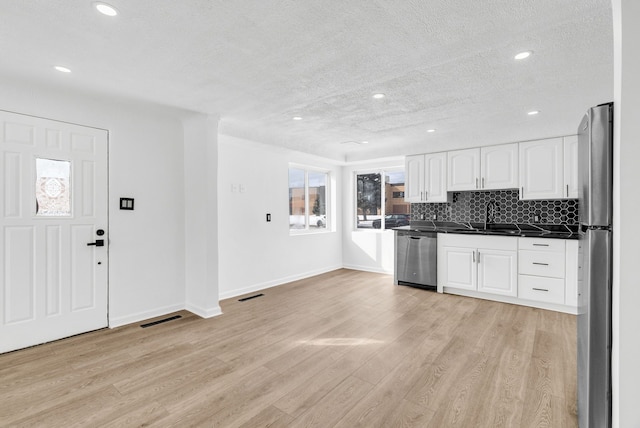 kitchen with stainless steel appliances, a sink, visible vents, light wood-style floors, and dark countertops