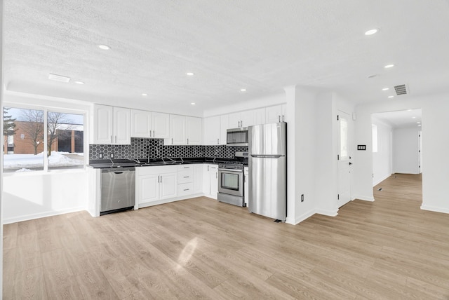 kitchen with white cabinets, dark countertops, appliances with stainless steel finishes, light wood-type flooring, and backsplash