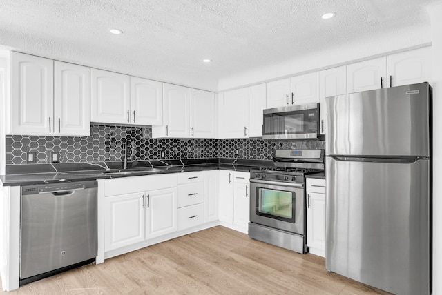 kitchen with appliances with stainless steel finishes, dark countertops, a sink, and light wood-style floors