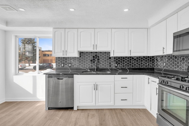 kitchen featuring stainless steel appliances, dark countertops, a sink, and light wood-style flooring