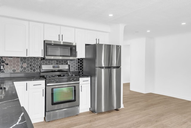 kitchen featuring light wood-style flooring, white cabinets, appliances with stainless steel finishes, tasteful backsplash, and dark countertops