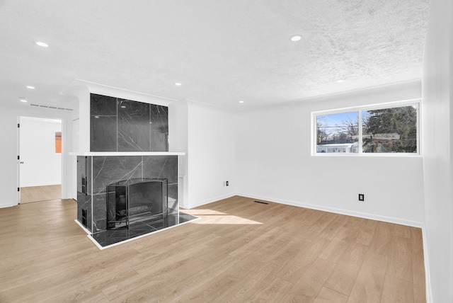 unfurnished living room featuring recessed lighting, a tiled fireplace, a textured ceiling, wood finished floors, and baseboards