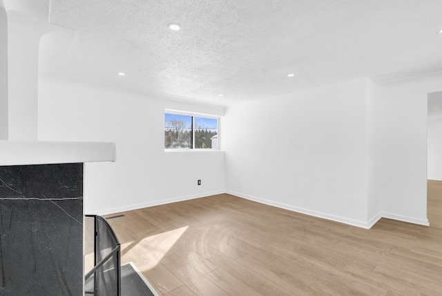 unfurnished living room with a textured ceiling, wood finished floors, and baseboards