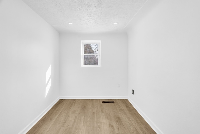 spare room featuring visible vents, a textured ceiling, baseboards, and wood finished floors