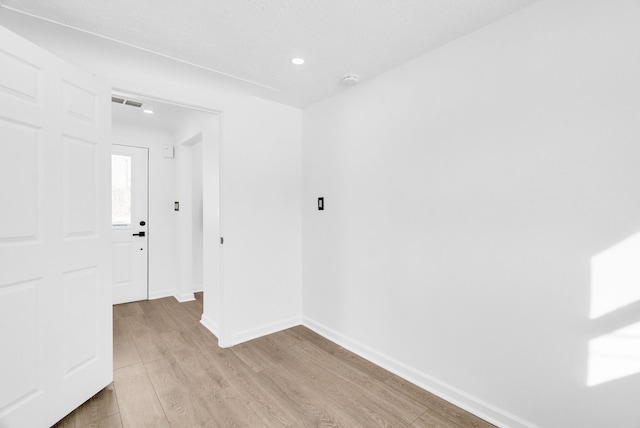 empty room with light wood-style floors, recessed lighting, visible vents, and baseboards