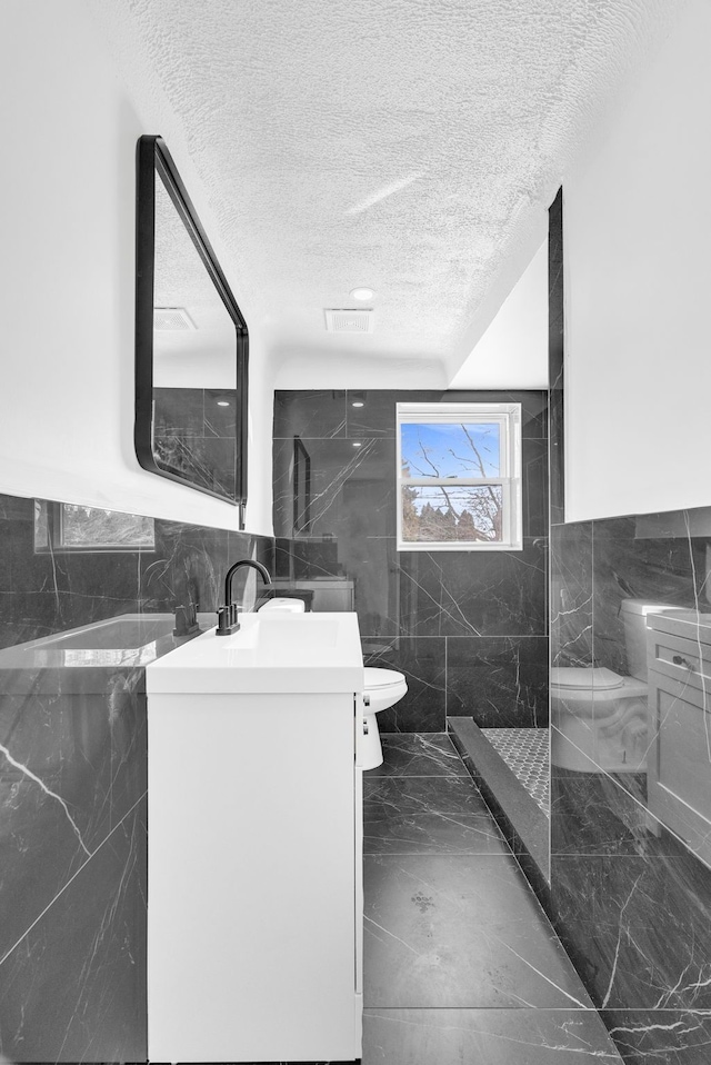 bathroom with visible vents, toilet, marble finish floor, a textured ceiling, and tile walls