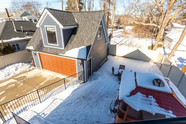 view of snowy exterior featuring an attached garage, fence private yard, and a shingled roof