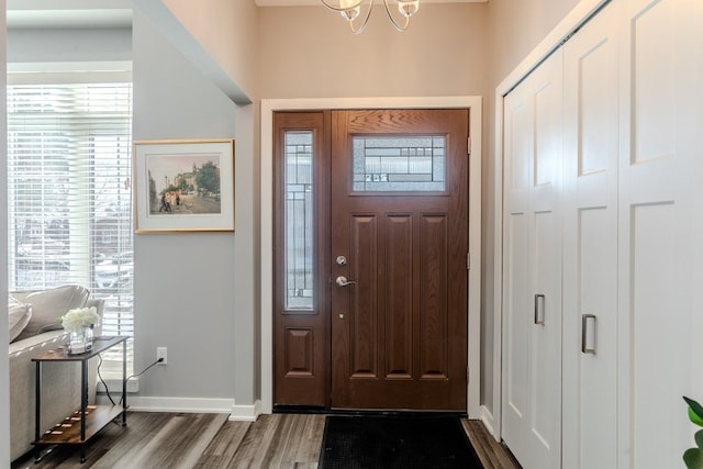 entryway with a wealth of natural light, a notable chandelier, dark wood-type flooring, and baseboards