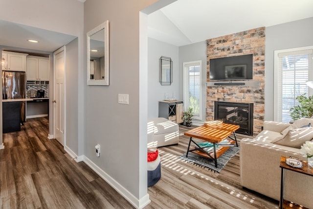 living room with dark wood finished floors, a stone fireplace, baseboards, and lofted ceiling