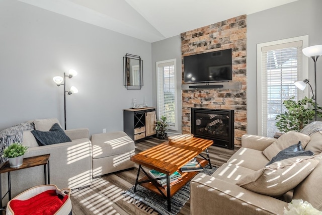 living area featuring a wealth of natural light, lofted ceiling, a stone fireplace, and wood finished floors