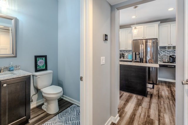 bathroom with vanity, wood finished floors, baseboards, toilet, and tasteful backsplash